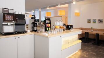 Un moderno café con máquinas de espresso, una estación de café y una zona de estar con sofá y mesa.