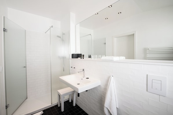Un baño moderno con cabina de ducha de vidrio, un lavabo blanco y un espejo grande.