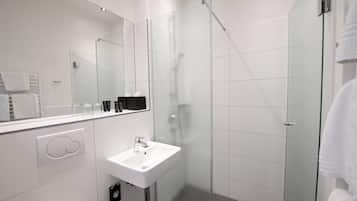 Un baño moderno con ducha envuelta en vidrio, lavamanos blanco y espejo grande.