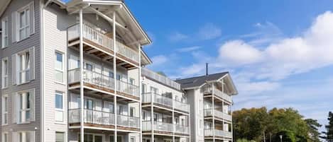 A multi-story hotel with balconies, a covered entrance, and a view of the sea.