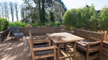 Una terraza de madera al aire libre con una mesa y dos bancos, rodeada de exuberante vegetación y árboles.