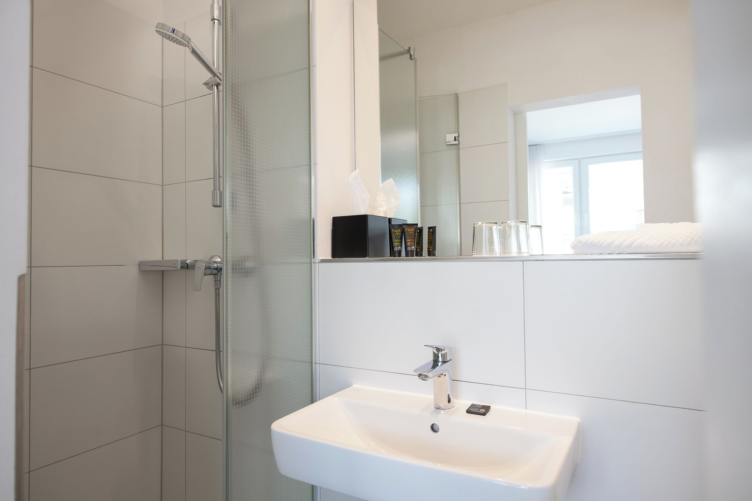 Ein modernes Badezimmer mit einer Duschkabine, einem weißen Waschbecken und einem Spiegel darüber.