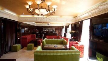 Eine geräumige Lounge mit grünen Polstersofas, einer Bar und einer Kristallleuchter.