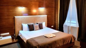 Quarto de hotel com uma cama grande, cabeceira de madeira e uma janela com cortinas.