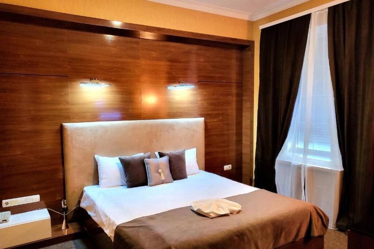 A hotel room with a large bed, wooden headboard, and a window with curtains.