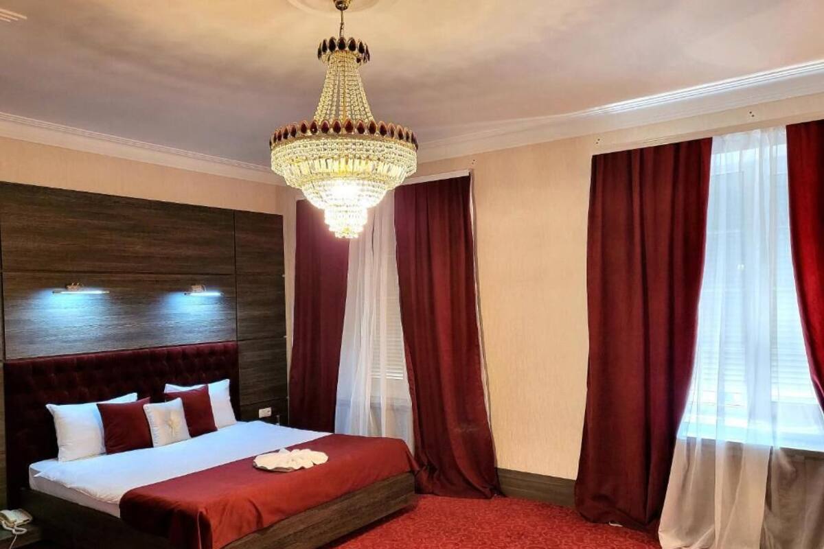 A hotel room with a large bed, a chandelier, red curtains, and a red carpet.
