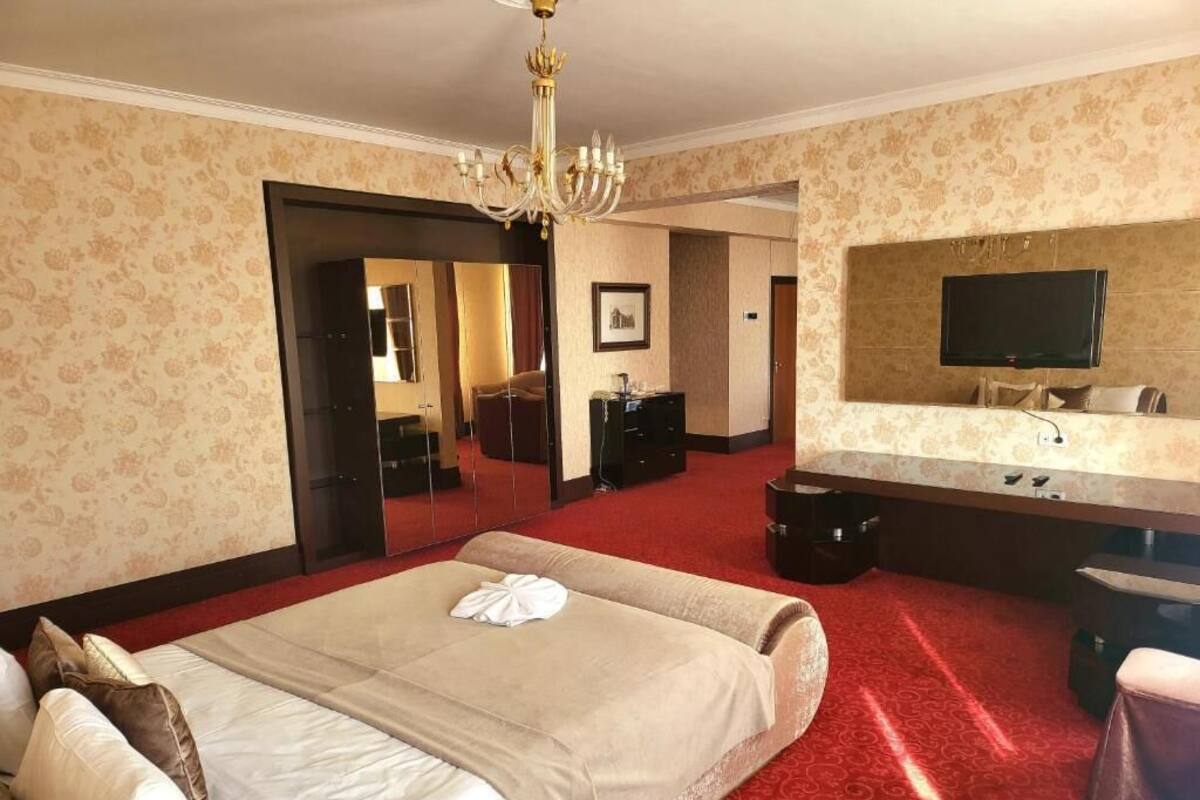 A hotel room with a large bed, a chandelier, a television, and a mirror.