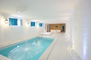 A modern indoor pool with a clear blue water feature, white walls, and a seating area with white furniture. - Maxim Pasha Hotel (Chisinau)