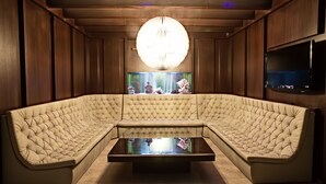 Uma área de estar moderna e luxuosa com um sofá grande e estofado, uma mesa de centro e um imponente candelabro circular.