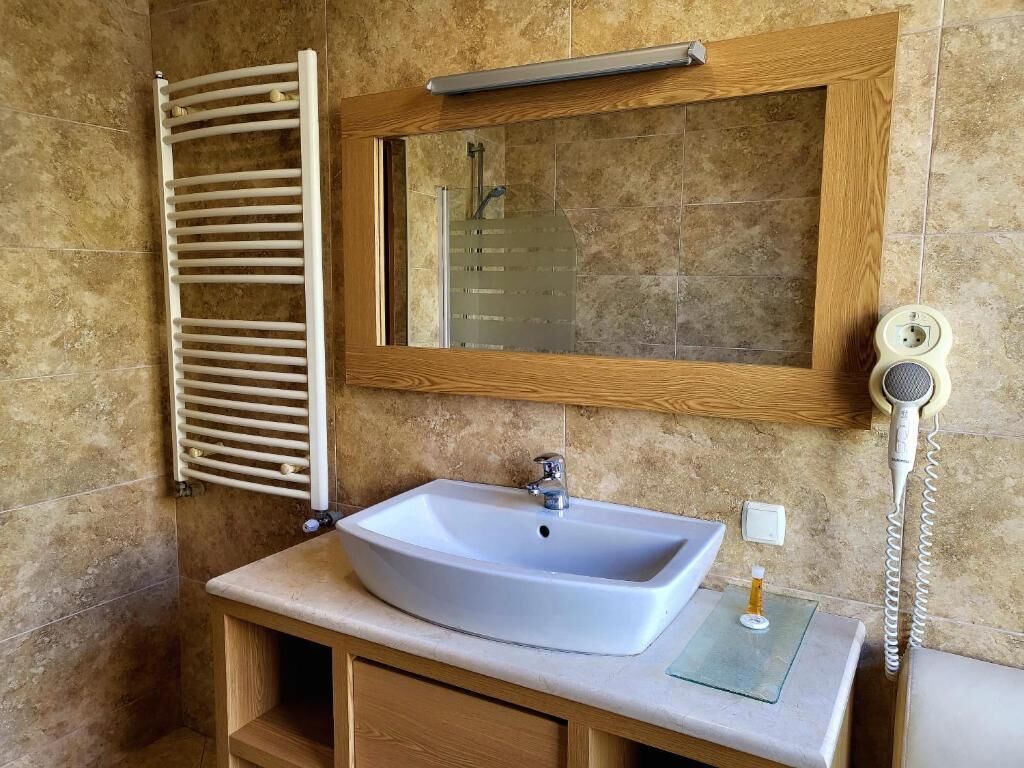 A bathroom with a white sink, wooden vanity, a towel rack, a mirror, and a hairdryer.