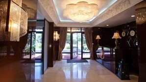 Um hall amplo com um lustre imponente, janelas grandes e piso lustroso.