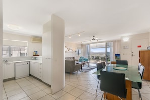 A modern kitchen with a dishwasher, a dining area with a glass table, and a view of the city.