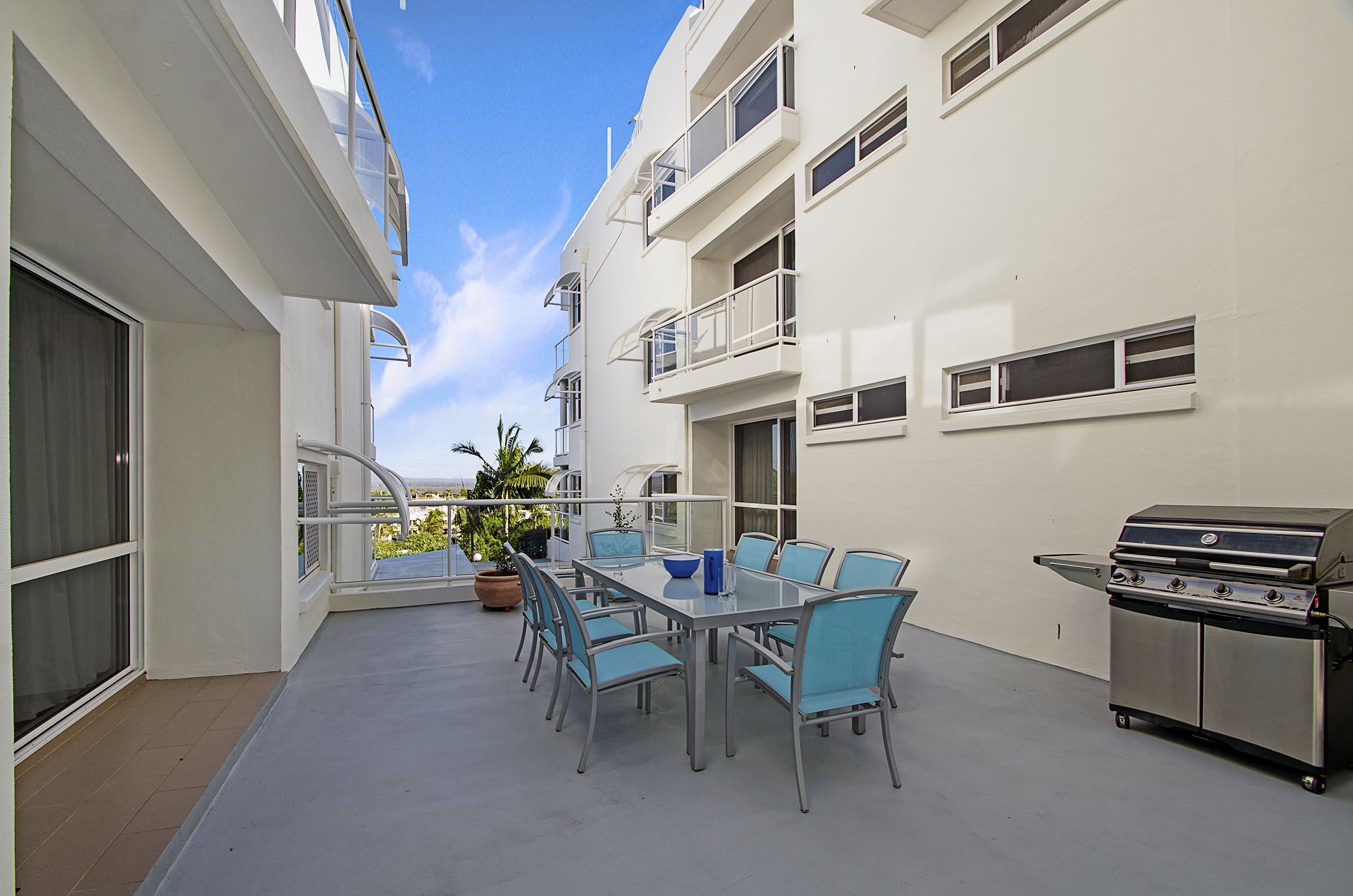 Ein Balkon mit Tisch, Stühlen, einem Grill und Blick zum Himmel.