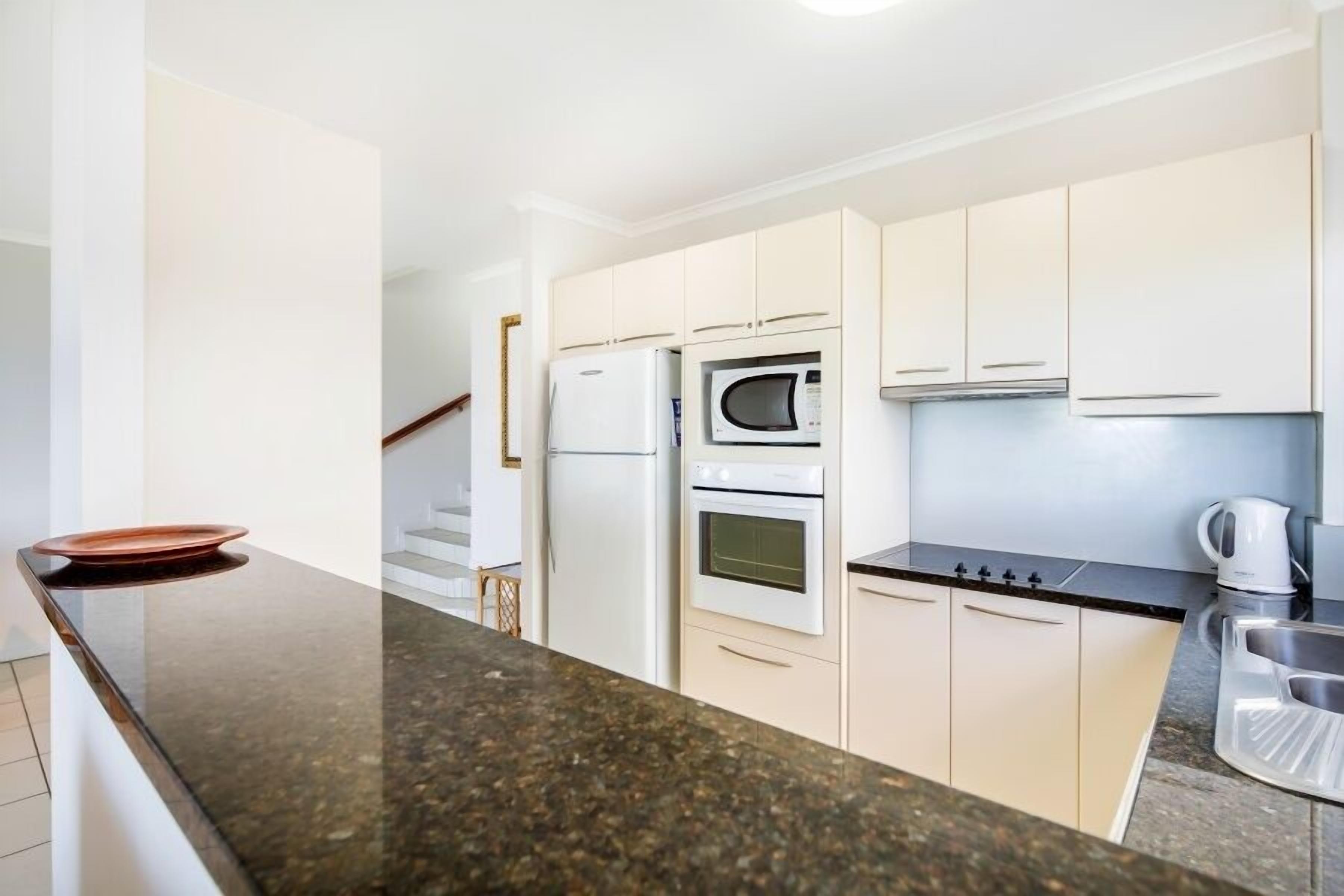 Una cocina moderna con armarios blancos, encimera negra, microondas, refrigerador y horno.