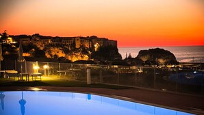 Piscina con vista a la puesta de sol sobre un edificio histórico y la costa.
