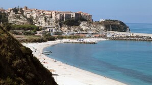 Un pueblo costero con un edificio histórico en un acantilado, una playa de arena y barcos en el agua.
