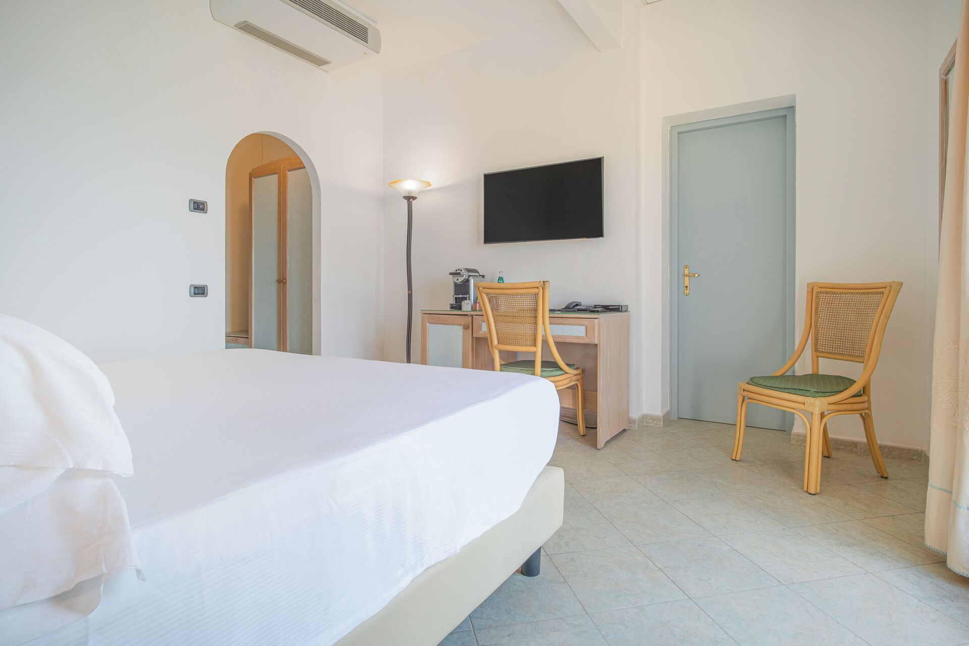 Une chambre d’hôtel avec un lit, un bureau et une chaise, une télévision et une porte.