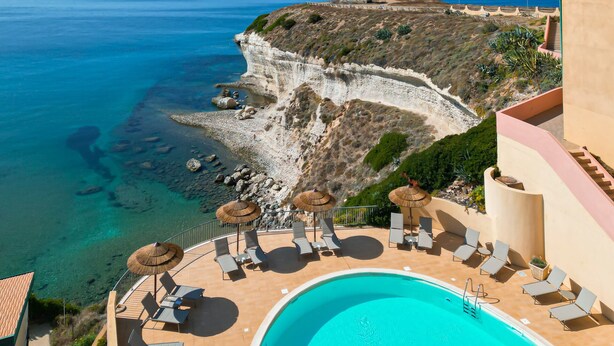 Un resort con piscina, sillones de descanso y vista al mar.