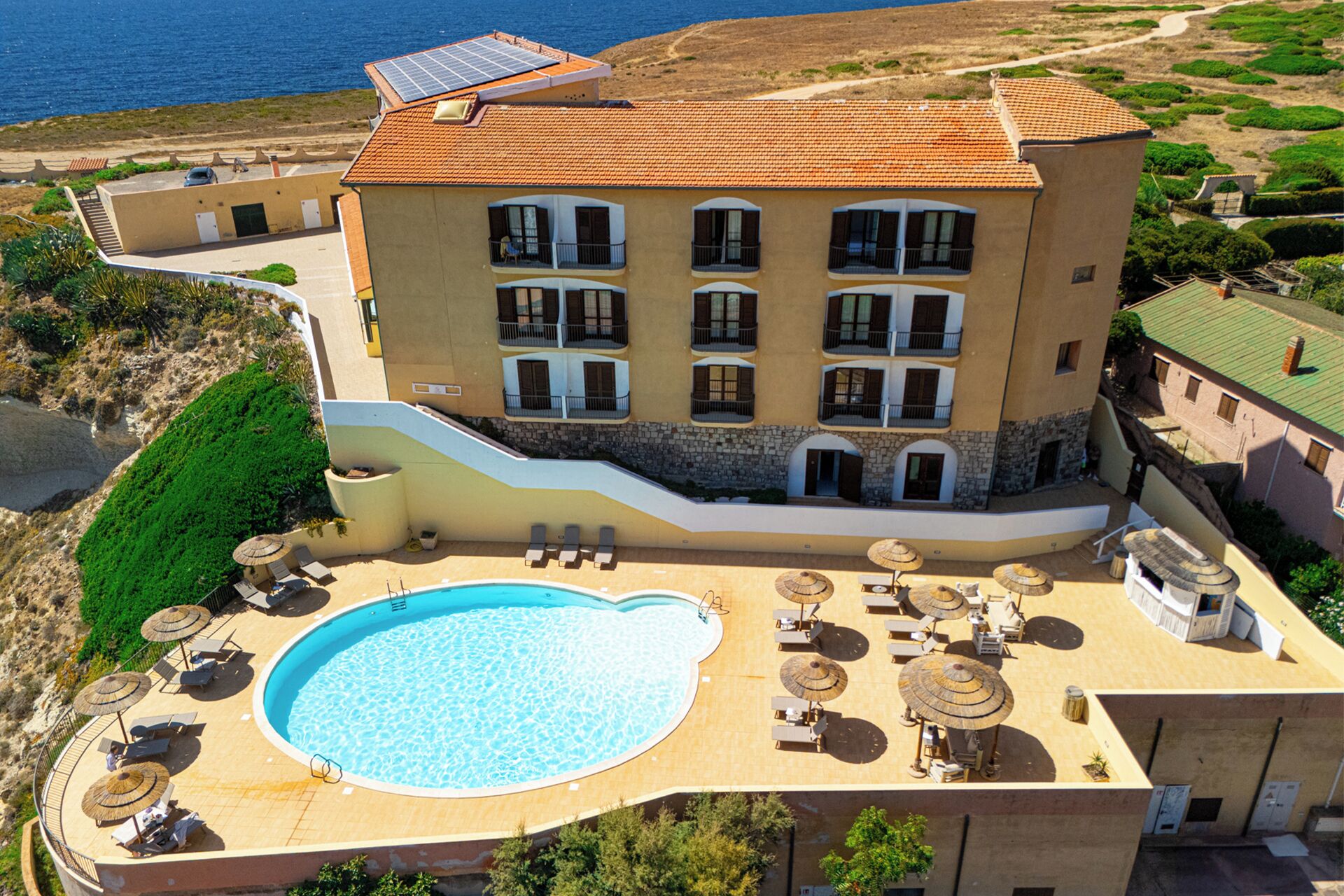 A multi-story hotel with a swimming pool, sun loungers, and umbrellas.