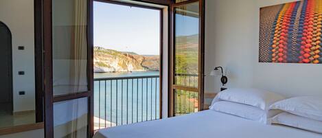 A bedroom with a large bed, a view of the sea, and a painting on the wall.