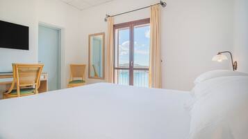 Une chambre d’hôtel comprenant un lit, un bureau, deux chaises, une télévision, une fenêtre avec des rideaux et une table de chevet avec une lampe.