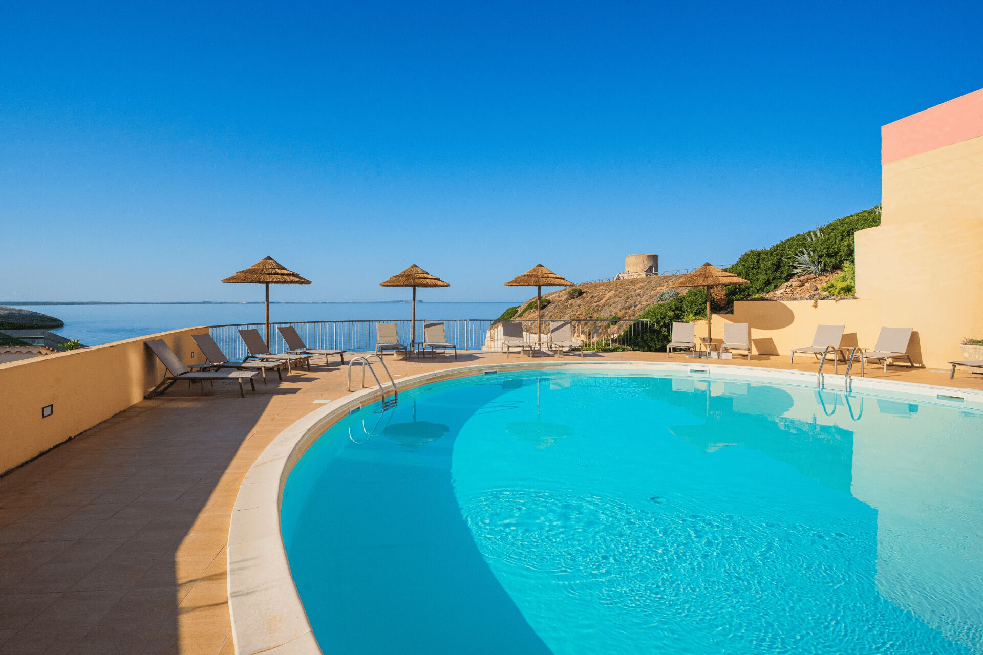 Ein Poolbereich mit Liegestühlen und Sonnenschirmen mit Blick auf ein Gewässer.
