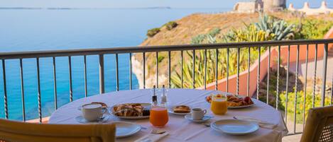 A table set for breakfast with a view of the sea and a historic building in the background.