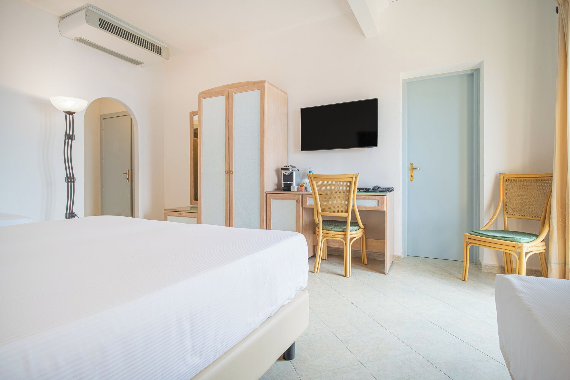 A hotel room with a bed, a desk with a chair, a television, and a door.