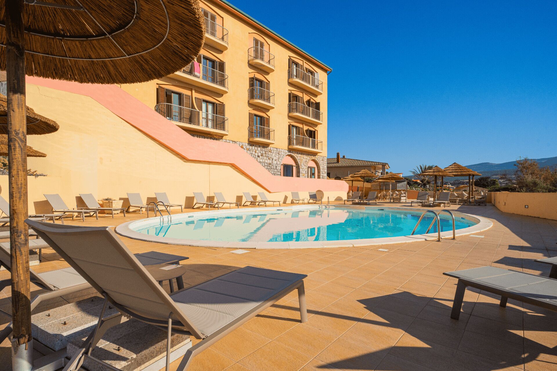 Un área junto a la piscina con sillones de descanso, una piscina y un edificio con balcones.