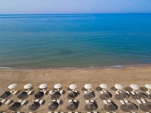 A beach with rows of sun loungers and umbrellas, a sandy shore, and the ocean in the background.
