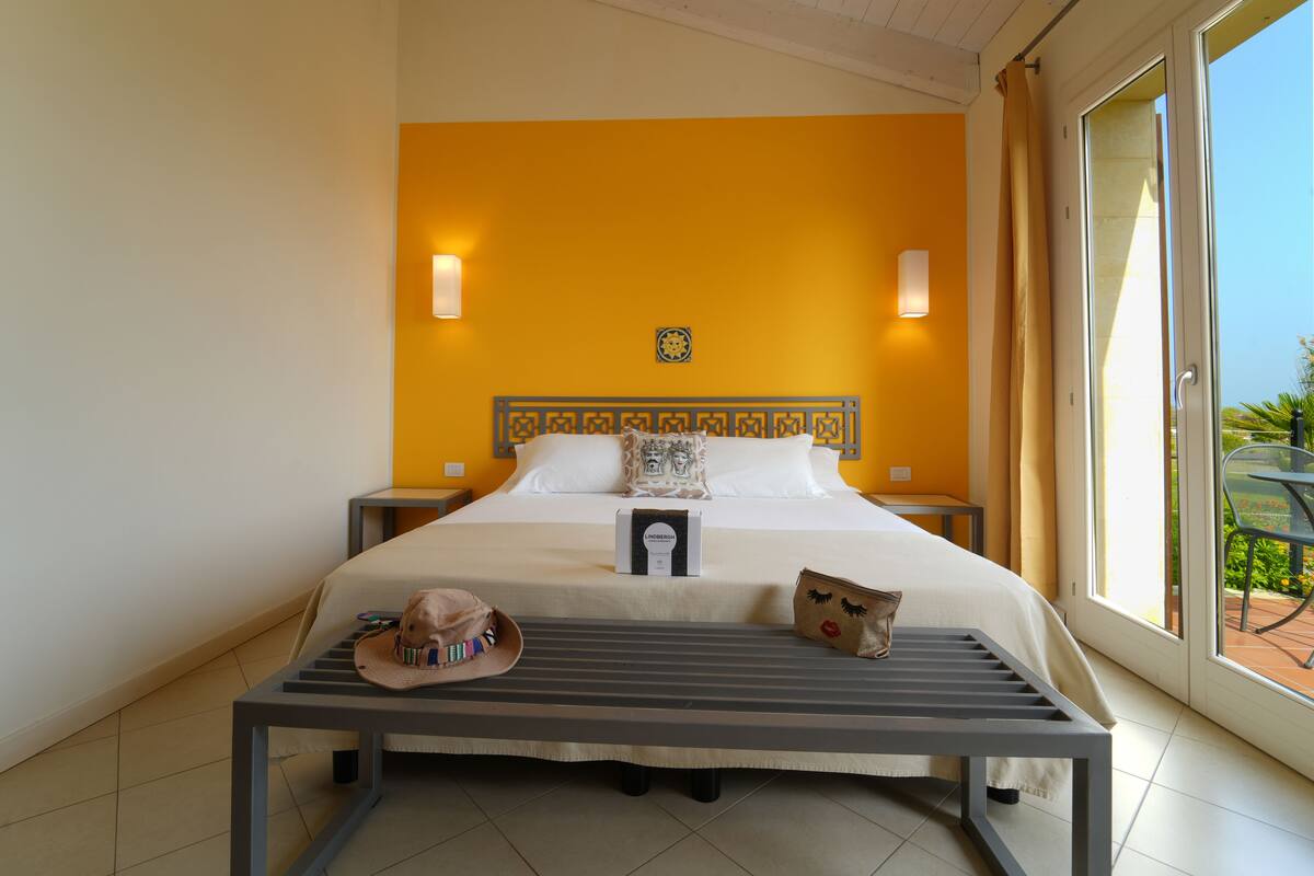 Habitación de hotel con cama, mesitas de noche, ventana con cortinas y vista al exterior.