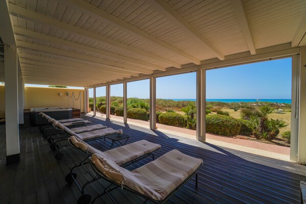 A covered outdoor lounge area with multiple sunbeds and a view of the beach.