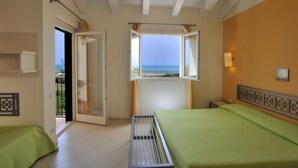 A room with two beds, a window with a view of the sea, a door leading outside, and a wall-mounted light fixture. - Zeta Club Sikania Eco Resort (Butera)