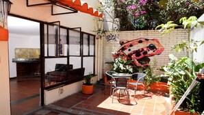 Un patio al aire libre con suelo de ladrillo, una mesa con sillas, plantas en macetas y una pared con un mural de mariquita.