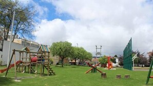 Un parque infantil con diversas estructuras de juego, incluyendo un tobogán y juegos de escalada, rodeado de césped y árboles.