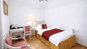 A bedroom with a bed, desk, chair, lamp, and a chandelier.