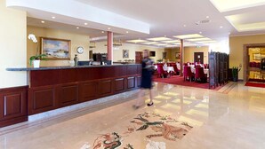 A hotel lobby with a reception desk, a clock, and a dining area with tables and chairs. - Brommavik Hotel (Bromma)