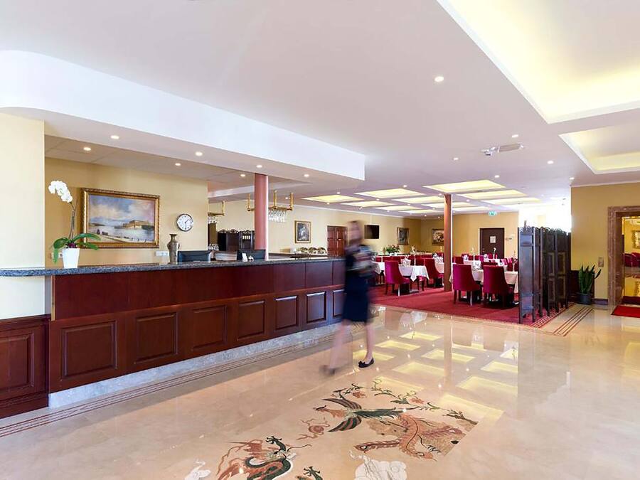 A hotel lobby with a reception desk, a clock, and a dining area with tables and chairs.