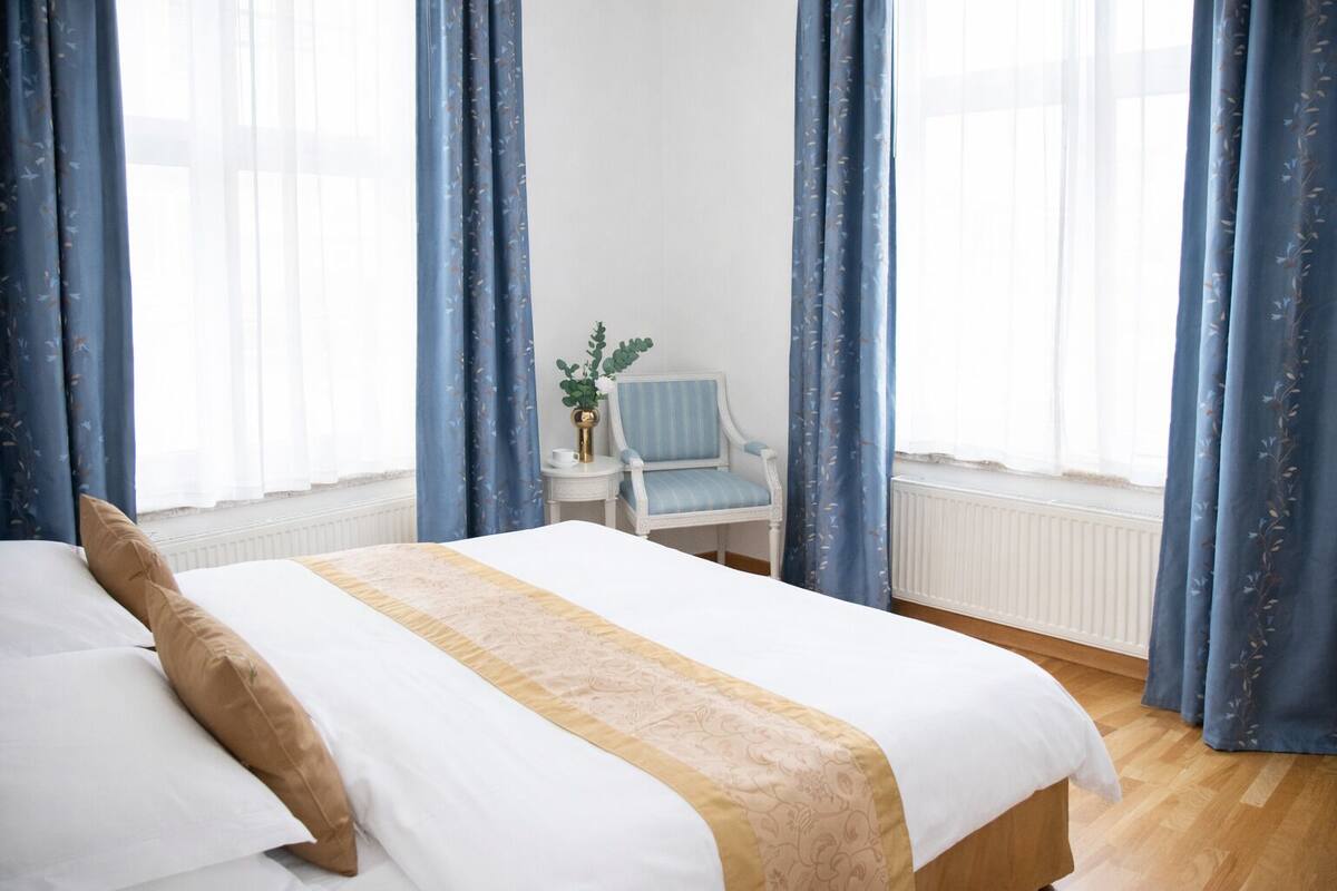 Una habitación de hotel con una cama, una silla y un ventanal con cortinas.