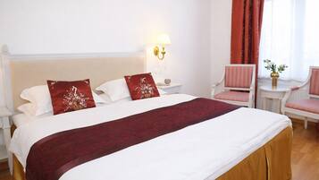Hotelkamer met een groot bed, nachtkastje, lamp, stoel en raam met gordijnen.