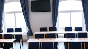 Un salón de conferencias con mesas y sillas, un proyector y un amplio ventanal con cortinas.