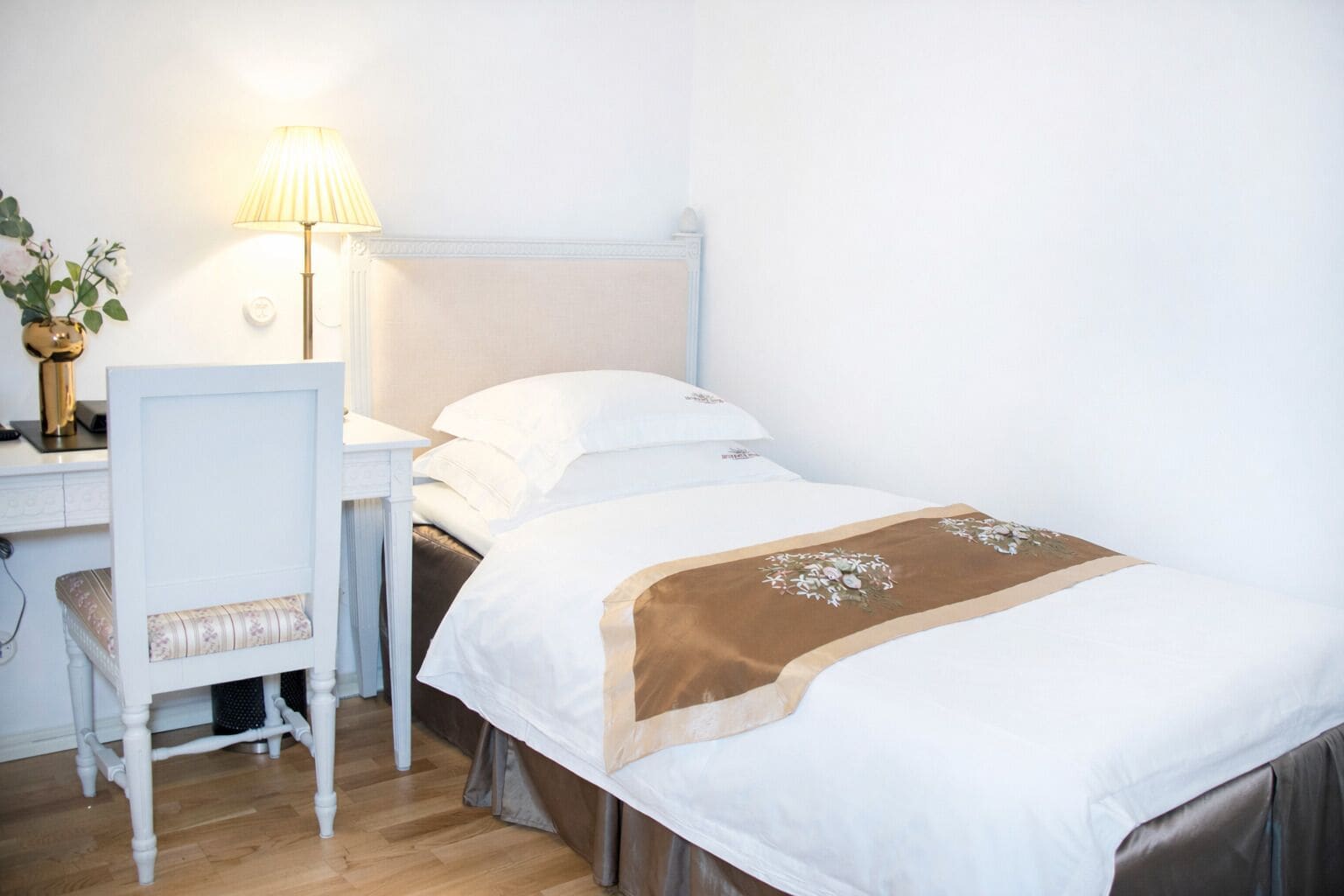 A hotel room with a bed, a desk with a lamp, and a chair.