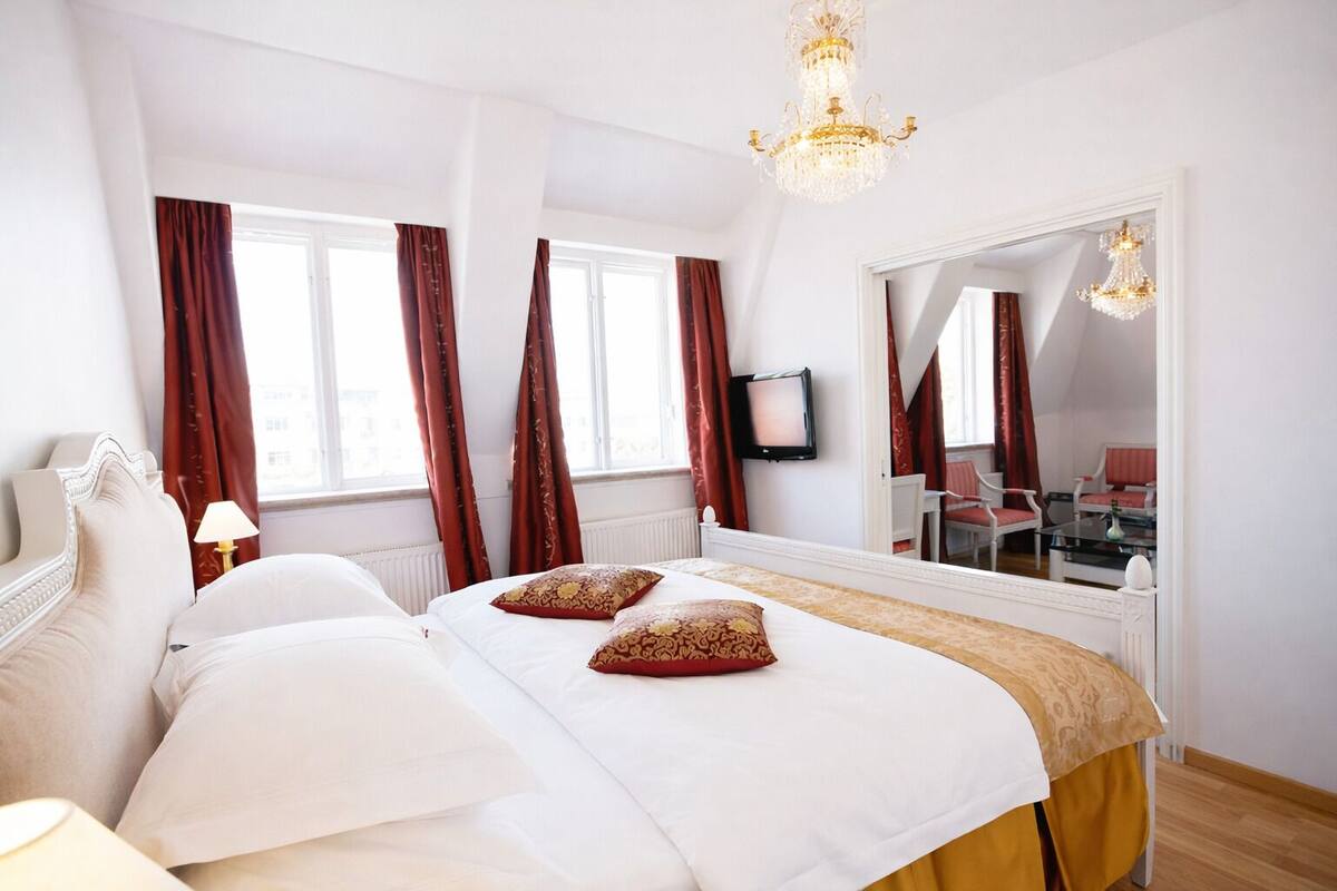 Una habitación de hotel con una cama grande, televisión, espejo y candelabro.