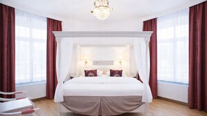 A four-poster canopy bed with a white headboard, two bedside lamps, and a red accent pillow. - Brommavik Hotel (Bromma)