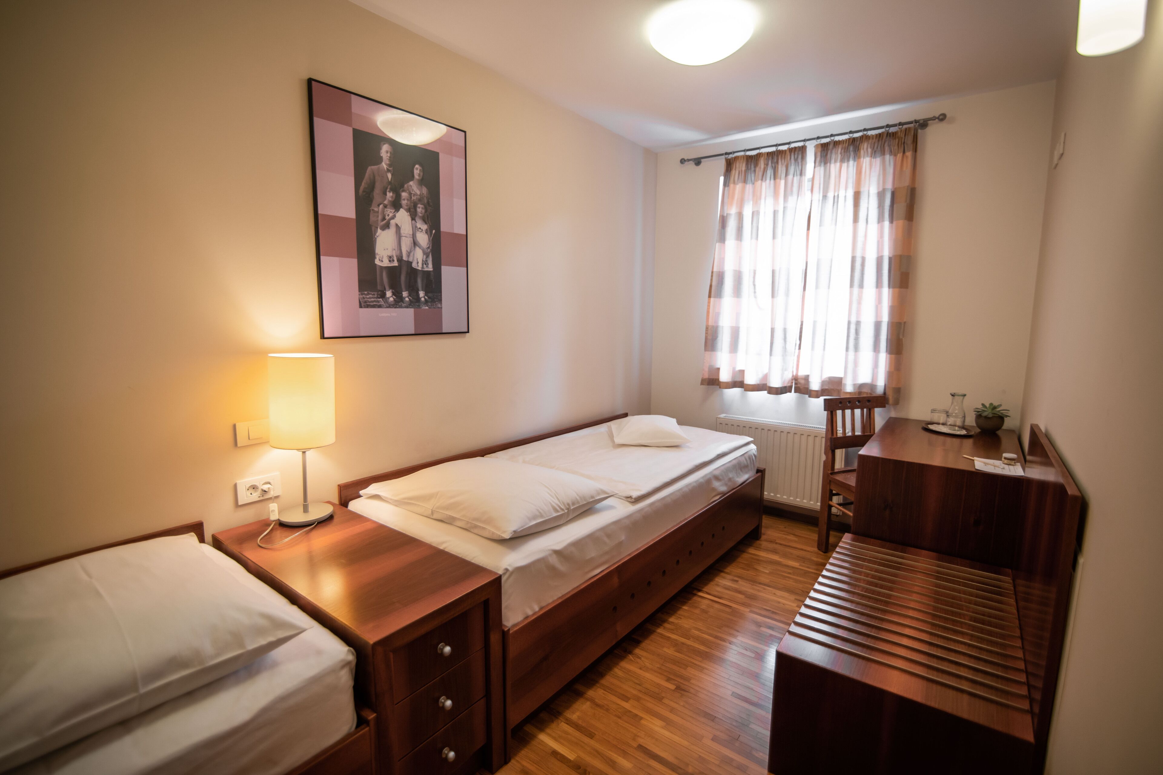 Een slaapkamer met een bed, nachtkastje, lamp en een raam met gordijnen.
