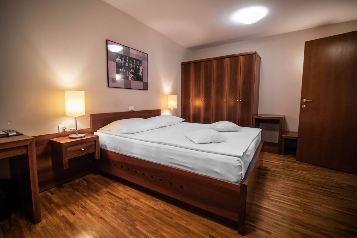 Ein ordentlich eingerichtetes Schlafzimmer mit einem hölzernen Bett, Nachttischen mit Lampen, einem Kleiderschrank und einem gerahmten Foto an der Wand.