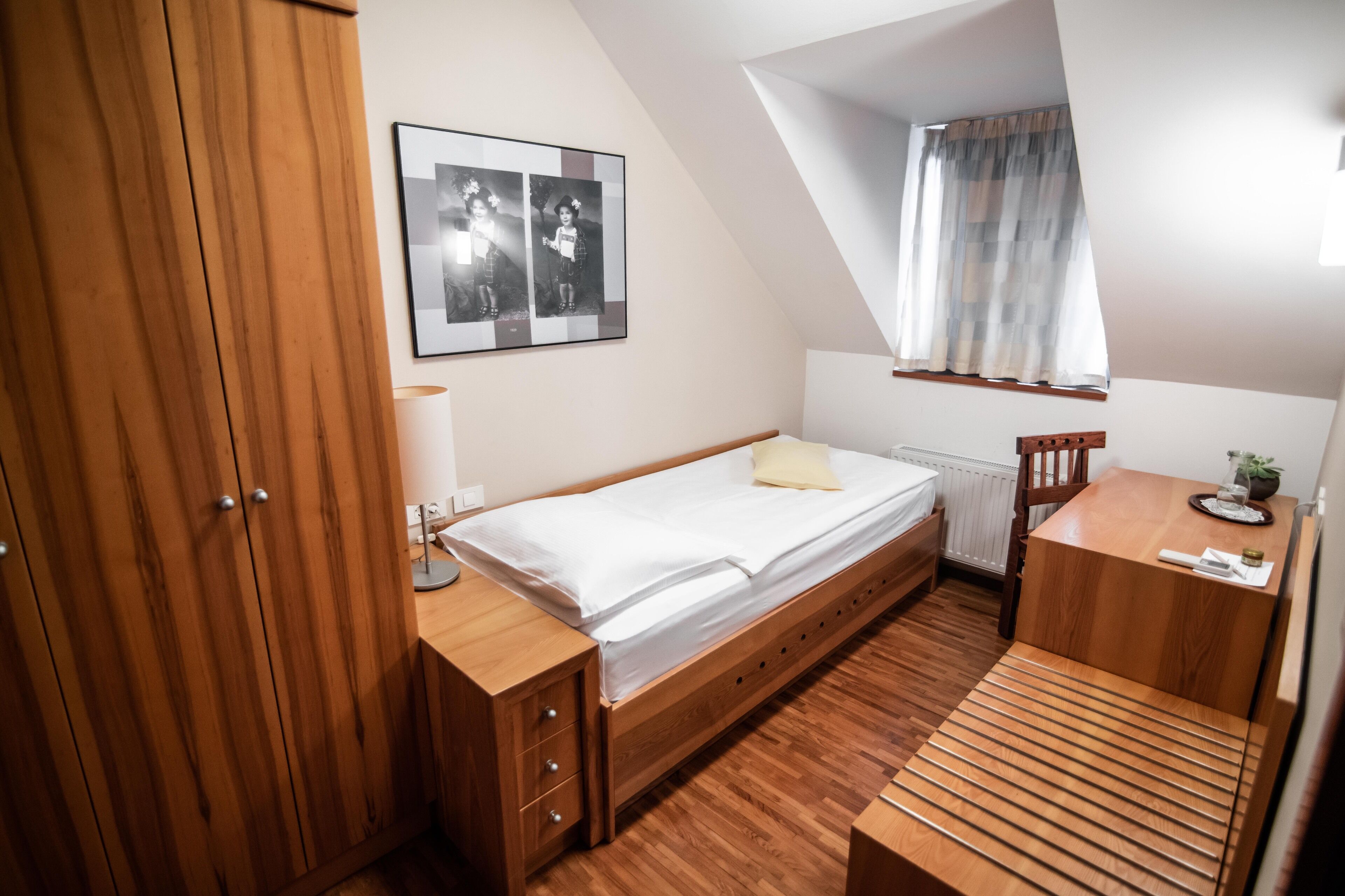 A bedroom with a wooden bed, a desk, a chair, and a window with curtains.