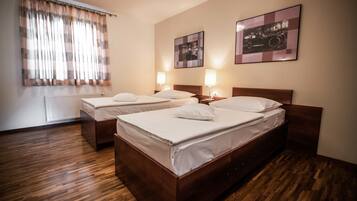 A hotel room with two wooden beds, a radiator, a window with curtains, and two wall-mounted lamps.