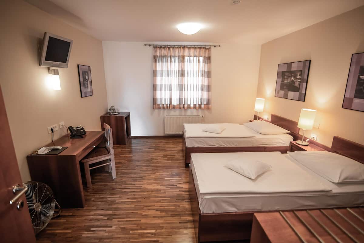 Ein Hotelzimmer mit zwei Betten, einem Schreibtisch mit Stuhl, einem Fernseher und einem Fenster mit Vorhängen.