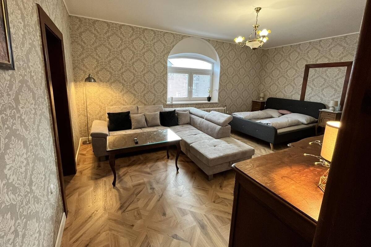 Ein Zimmer mit einer Couch, einem Bett, einem kleinen Tisch und einem Fenster mit Jalousien.